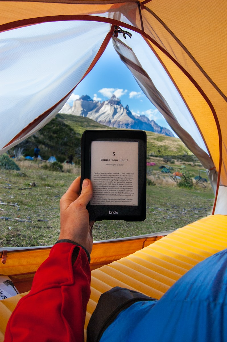 person holding black Amazon Kindle E-Book reader inside tent at daytime